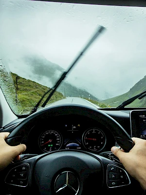 A driver’s view from inside a rain-soaked car cabin, steering through a misty mountain road with a rain-soaked windshield.