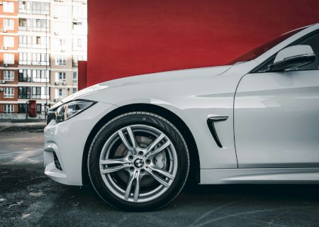 A close-up of a white sports car&rsquo;s front side with a red background, focusing on the wheel and fender, sleek and stylish.